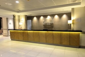 A reception desk with a wooden panel design, overhead lighting, and a tiled floor. - Holiday Inn Express Antofagasta by IHG (Antofagasta)