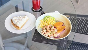 A meal consisting of a slice of pie with whipped cream, a bowl of salad with corn, chicken, and a slice of orange, and a glass of red juice on a glass table. - Holiday Inn Express Antofagasta by IHG (Antofagasta)