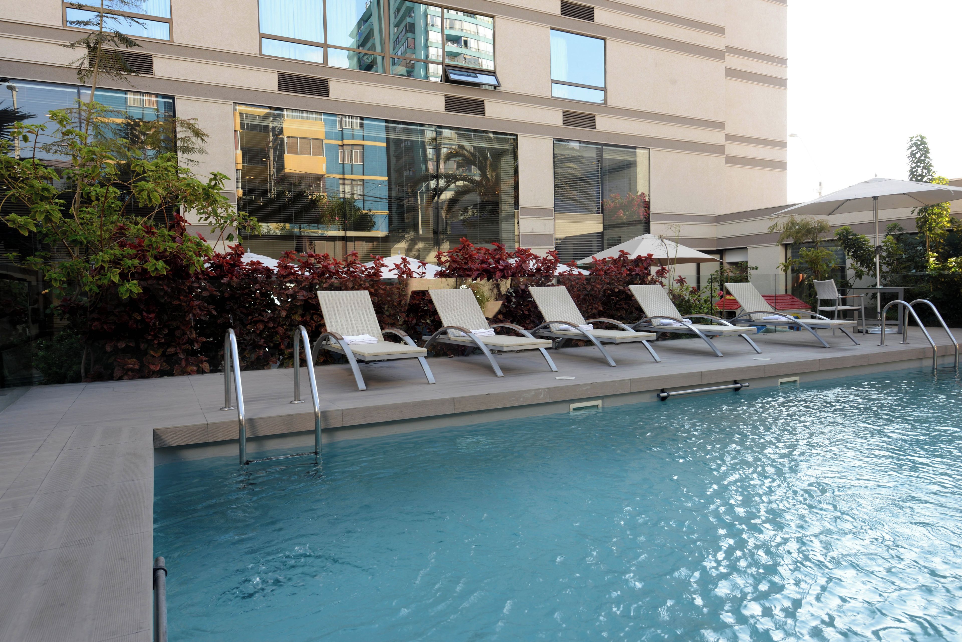 A poolside area with lounge chairs and umbrellas, surrounded by a building with large windows and a modern design.