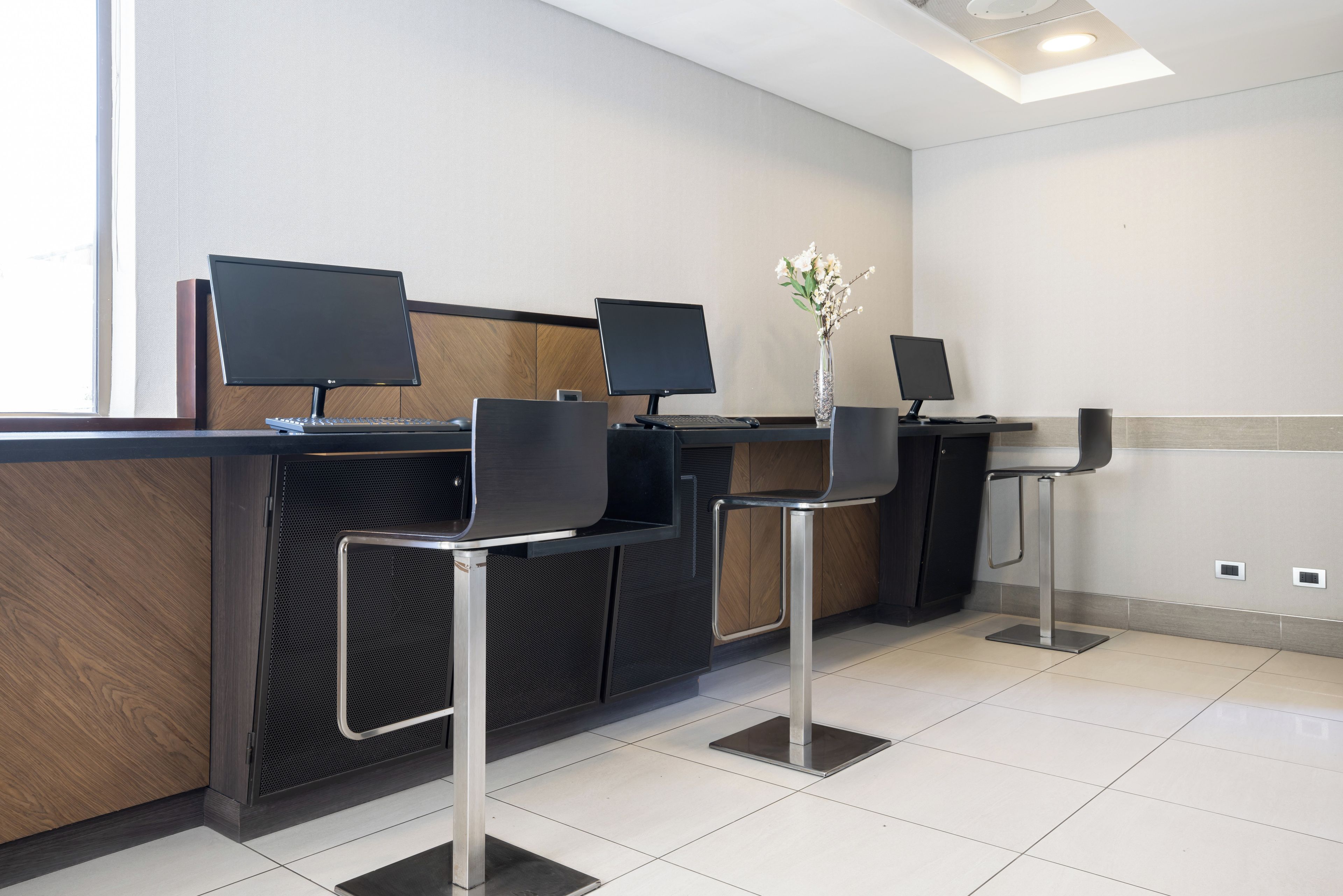 A reception area with three computer monitors, two chairs, and a vase with flowers.