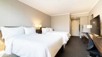 A hotel room with two beds, a desk with a chair, a television, and a door leading to a bathroom.