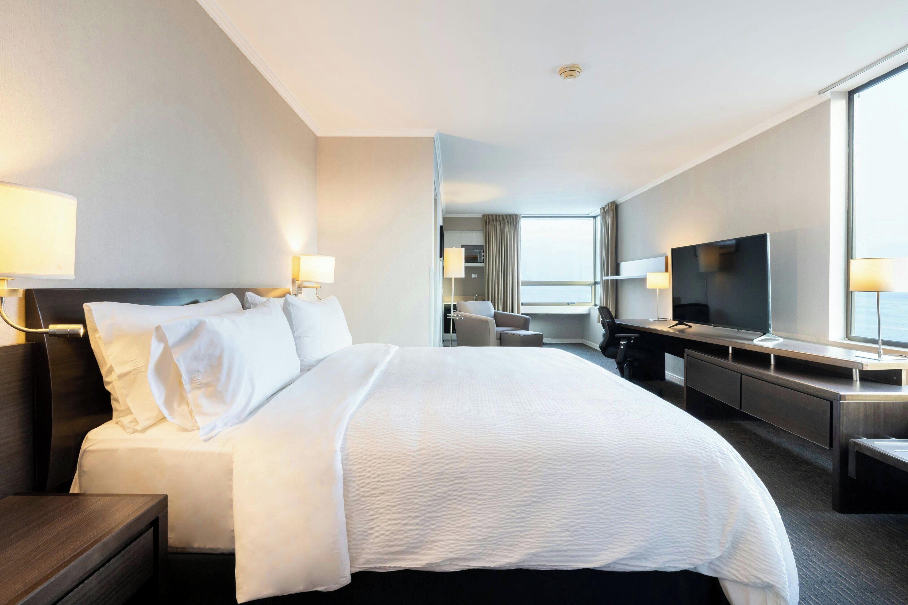 A hotel room with a large bed, a desk with a flat-screen TV, a chair, and a window with curtains.