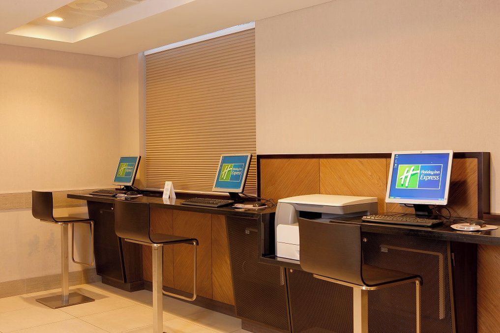 A hotel reception desk with three computer monitors, a printer, and two bar stools.