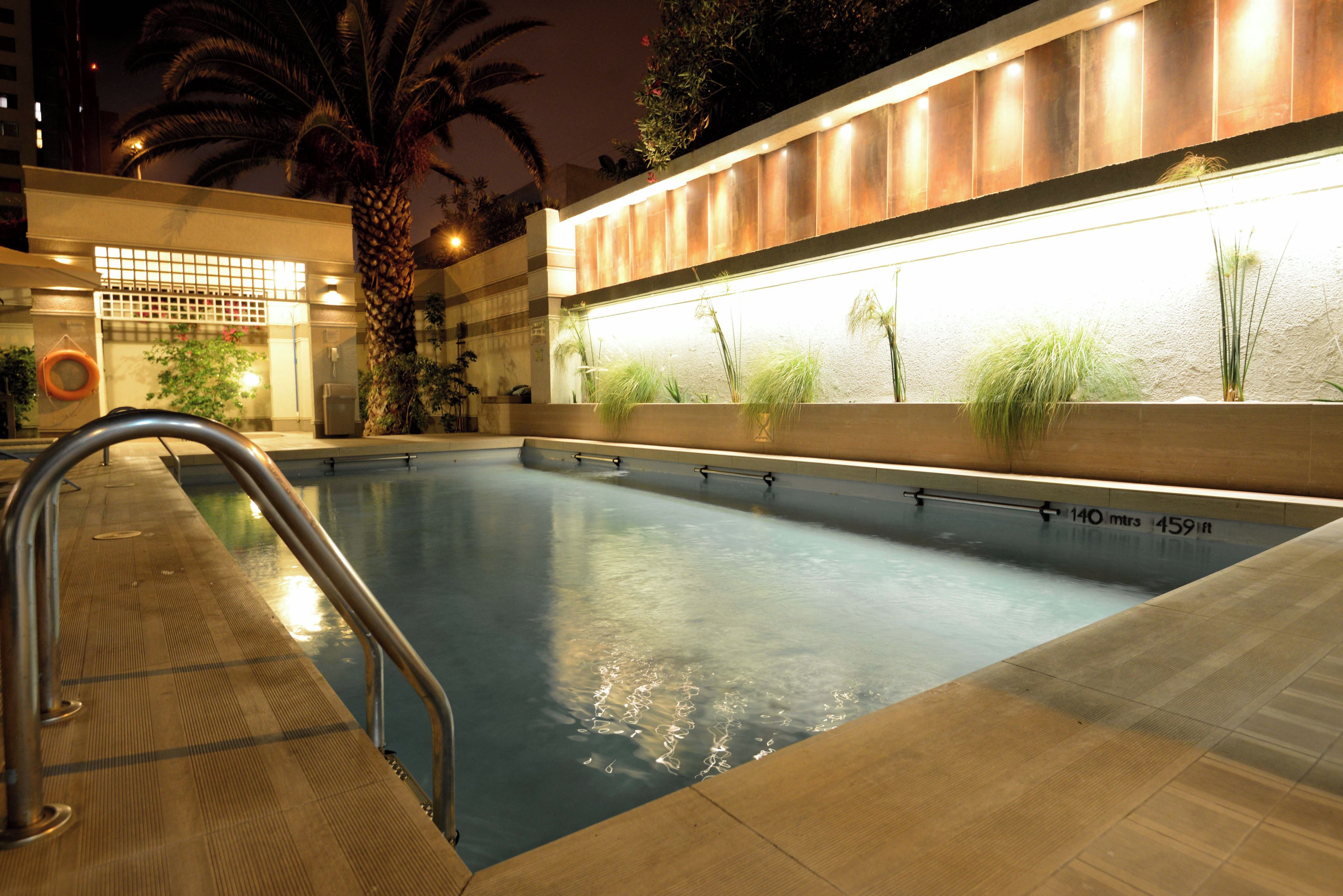 Una piscina con una escalera de metal, rodeada por un suelo de baldosas.