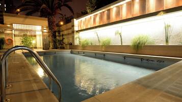 Una piscina con una escalera de metal, rodeada por un suelo de baldosas.
