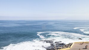 A coastal view with waves crashing against rocks, a clear sky, and a paved area with a railing. - Holiday Inn Express Antofagasta by IHG (Antofagasta)