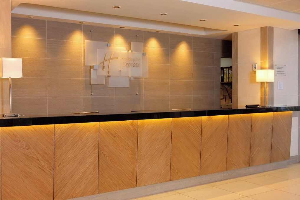 Un mostrador de recepción con detalles de madera y una encimera negra. Se observan señalizaciones en la pared y una lámpara a la izquierda.