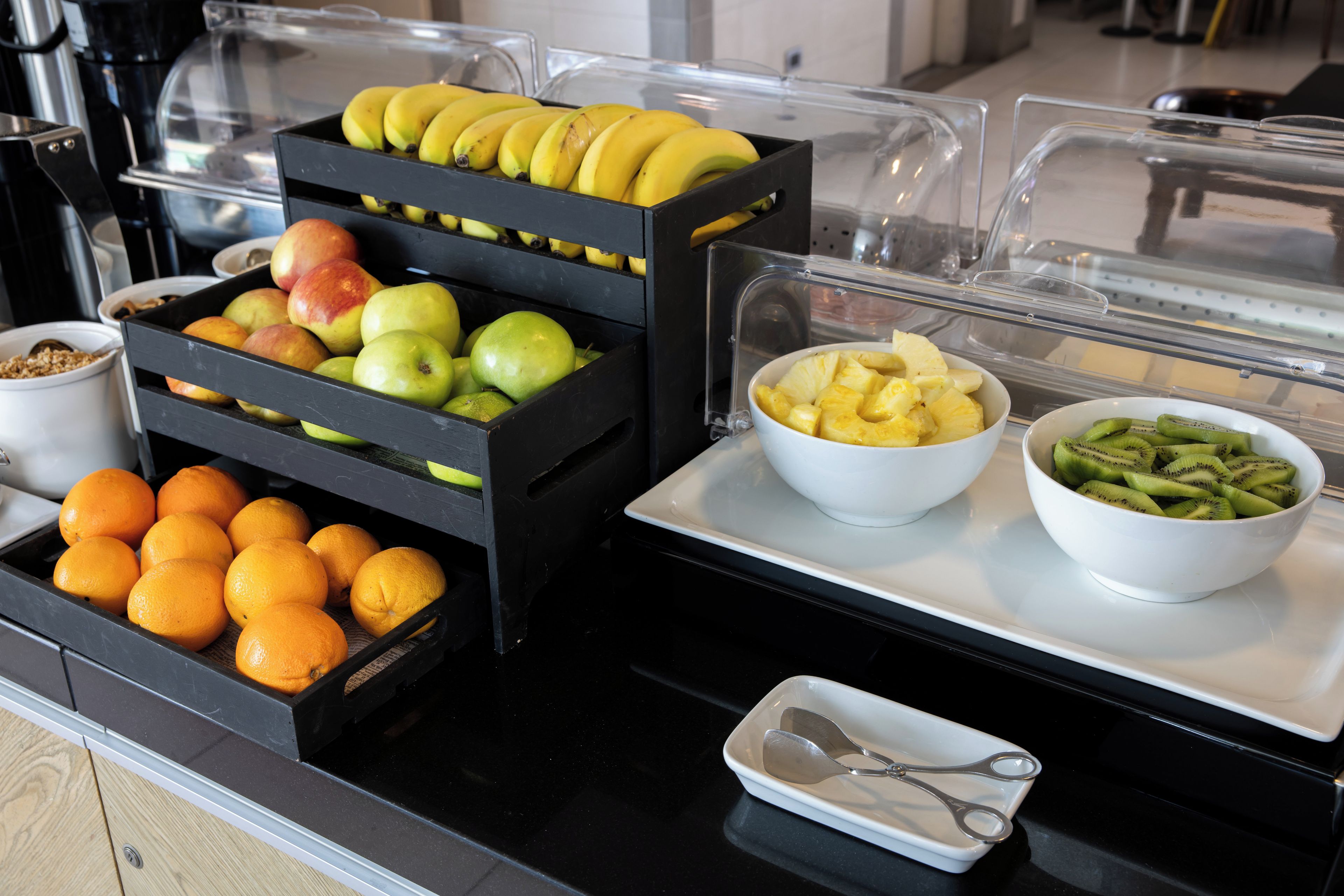 A buffet with various fruits and a pair of scissors on a tray.