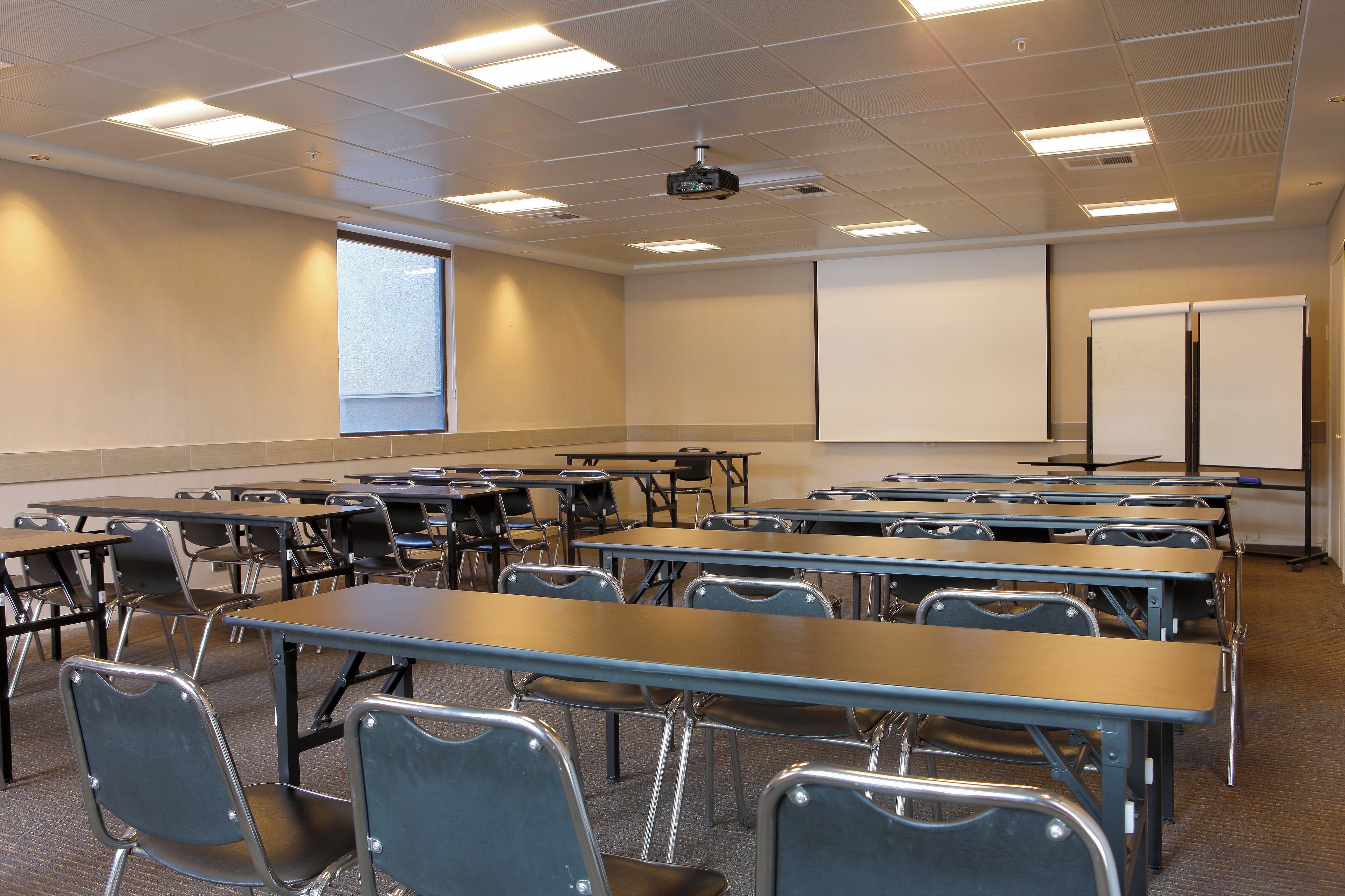 A classroom with desks, chairs, a projector, and a whiteboard.