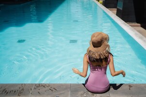 Una mujer sentada junto a una piscina con agua cristalina y azul.
