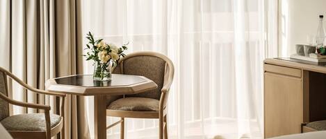 A hotel room with a bed, a wooden desk, a chair, and a table with a vase of flowers.