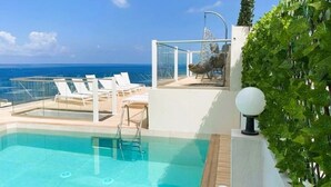 Una piscina en la azotea con agua azul cristalina, sillas de descanso blancas y vista al océano.