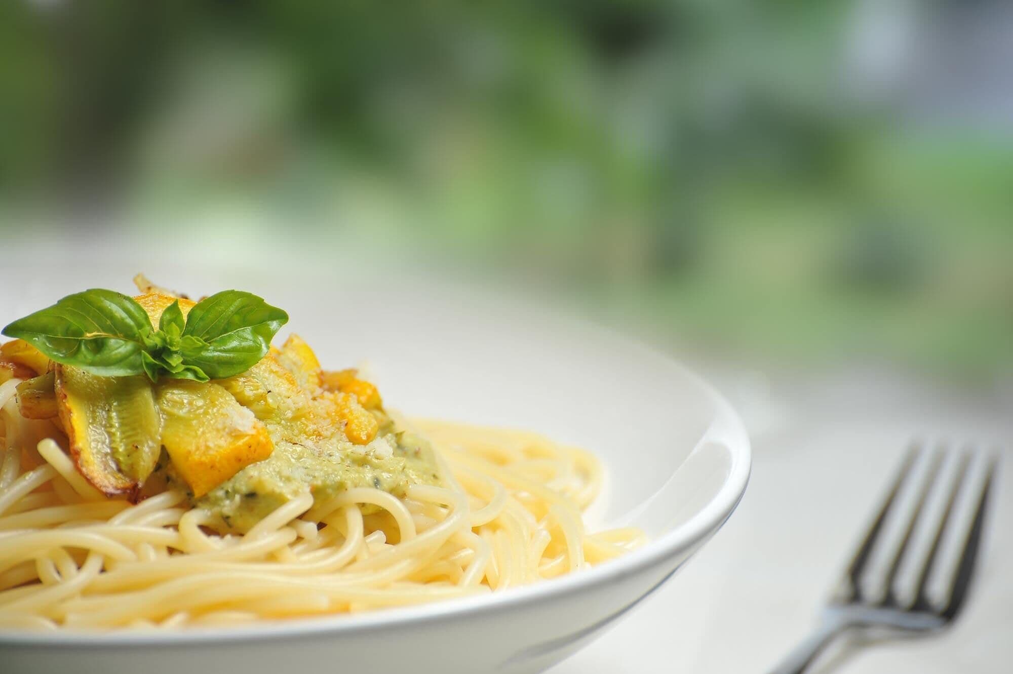 A plate of spaghetti with a green sauce and a basil leaf garnish.