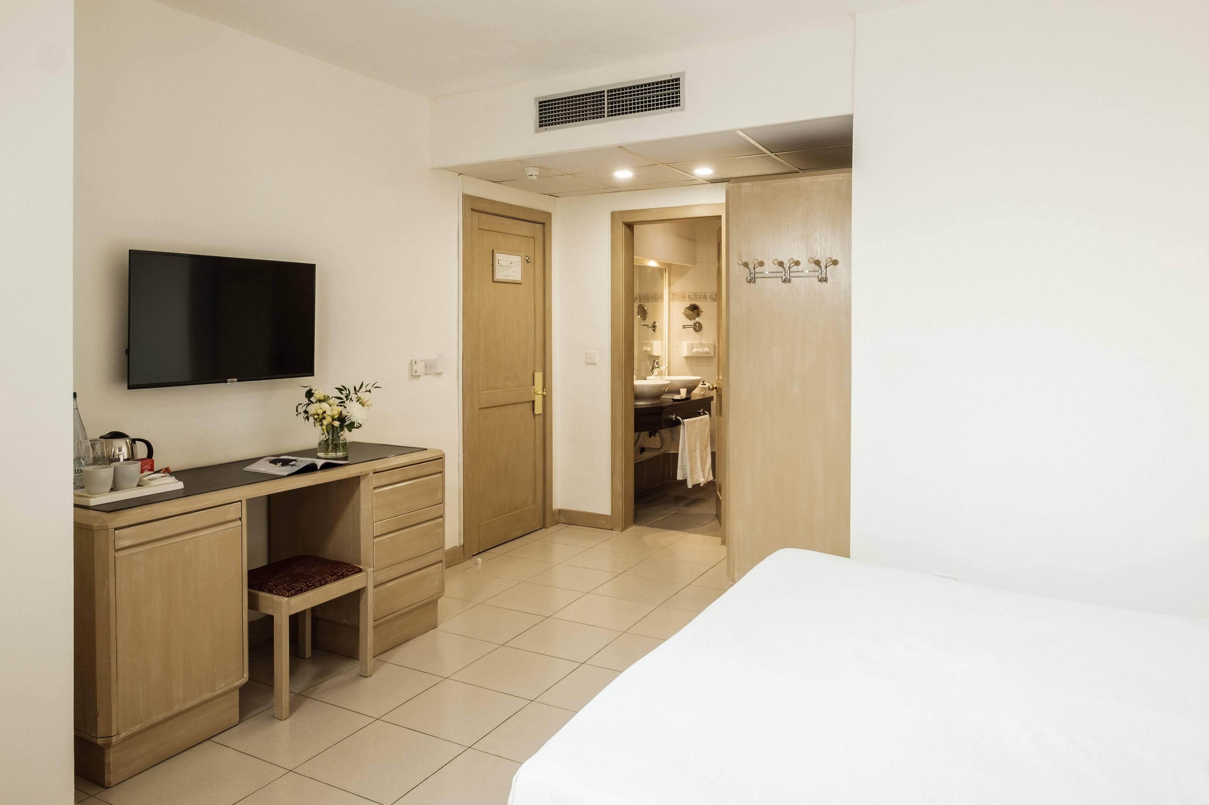Ein Hotelzimmer mit einem Bett, einem Schreibtisch mit Stuhl, einem Fernseher und einem durchgegangenes Badezimmer.