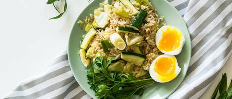 Un plato de arroz frito con verduras y dos mitades de huevo duro sobre un plato verde.