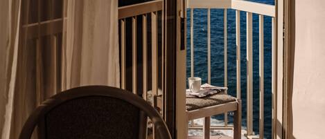 A balcony with a view of the ocean, a chair, and a table with a cup and a menu.