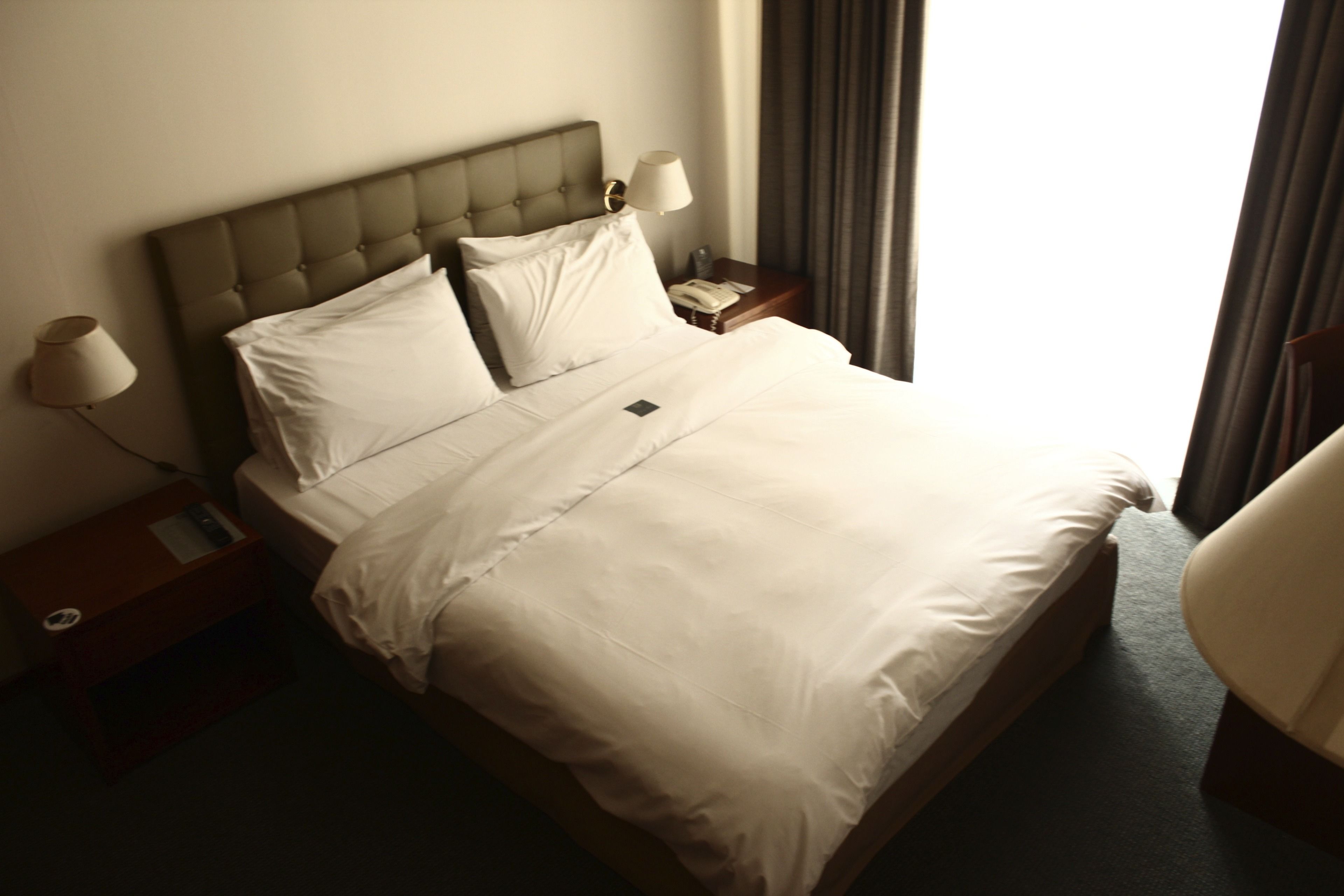 A neatly made bed with white linens, a wooden headboard, and bedside lamps.
