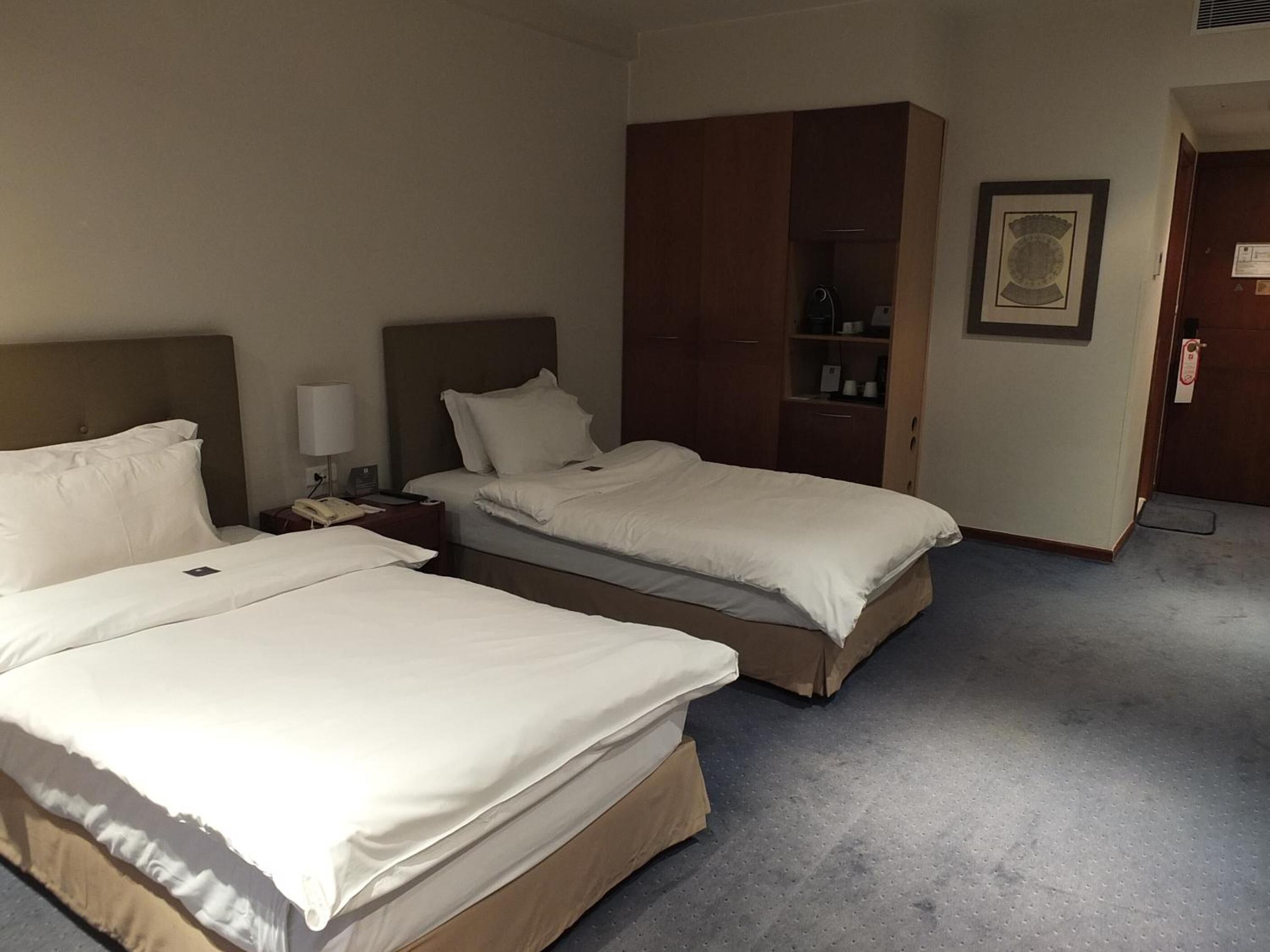 Habitación de hotel con dos camas, una mesita de noche, un armario y un certificado enmarcado en la pared.