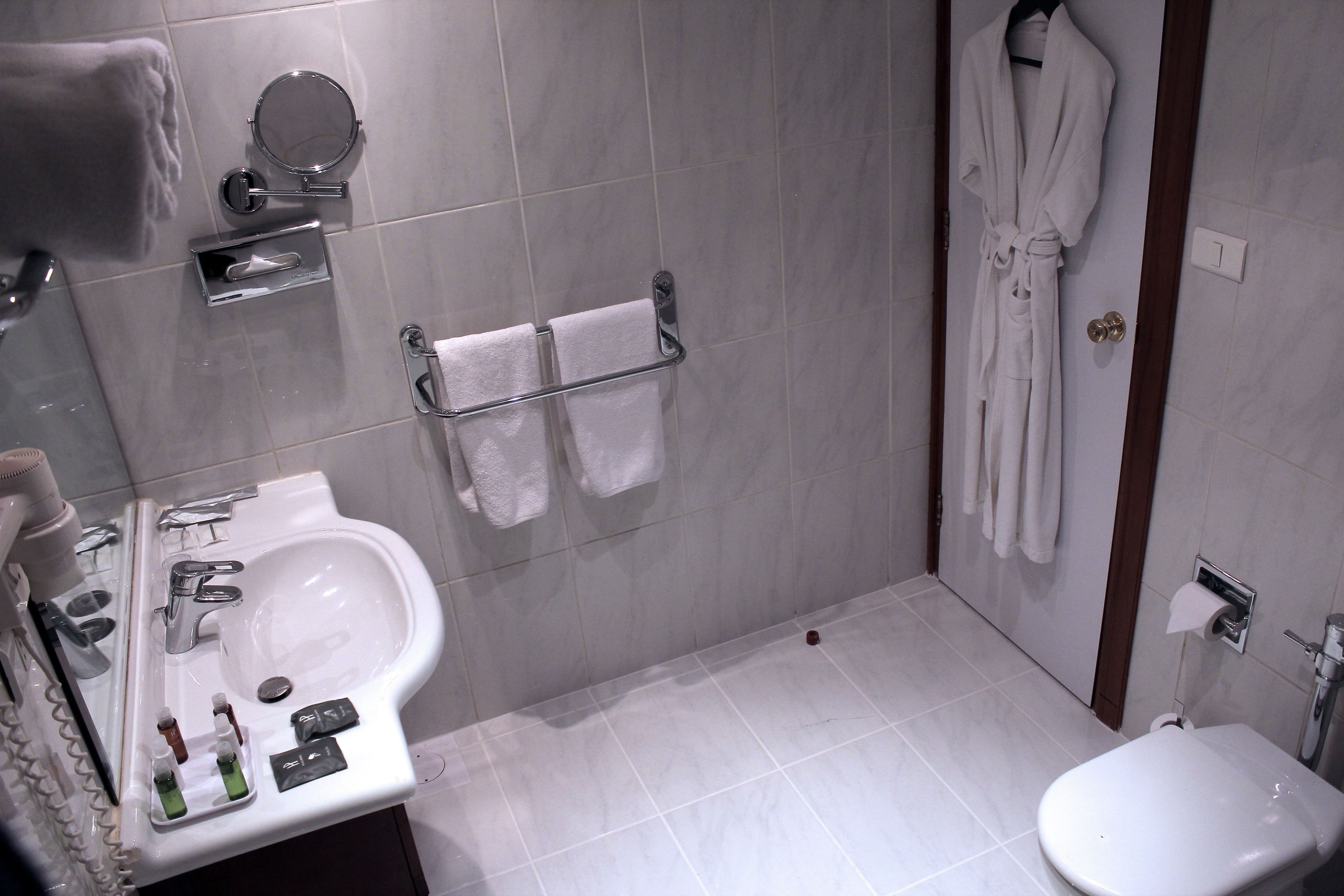 Un baño moderno con lavamanos, espejo, toallero y una bata colgada en la pared.