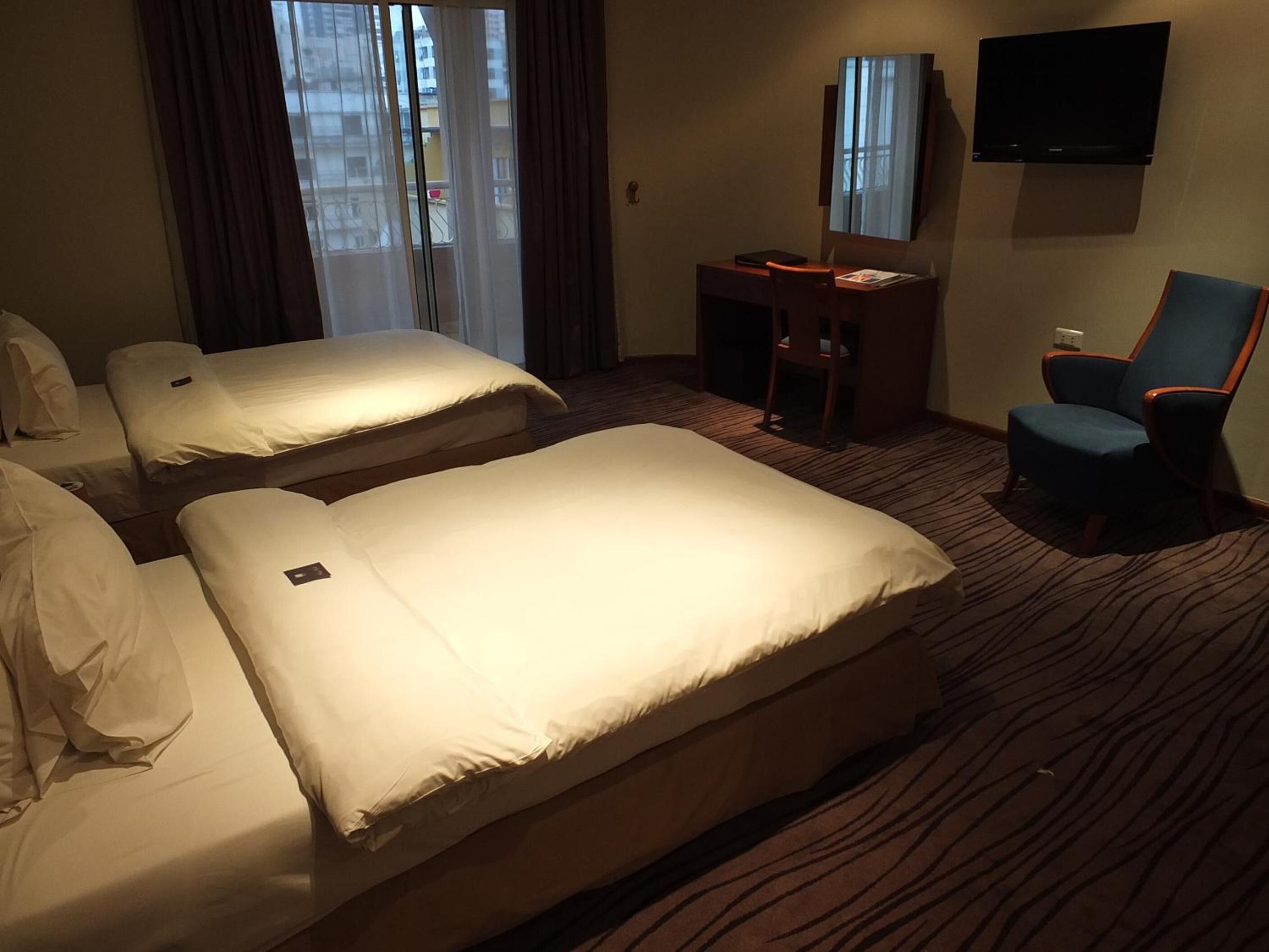 A hotel room with two beds, a desk, a chair, and a TV.