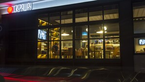 A hotel with a prominent sign reading "CREPAWAY". Inside, there are multiple dining areas with tables and chairs, and a bar area visible through the windows. - Plaza Hotel (Beirut)