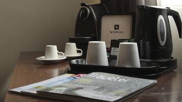 Una estación de café con una máquina Nespresso, vasos desechables y una revista sobre una mesa de madera.