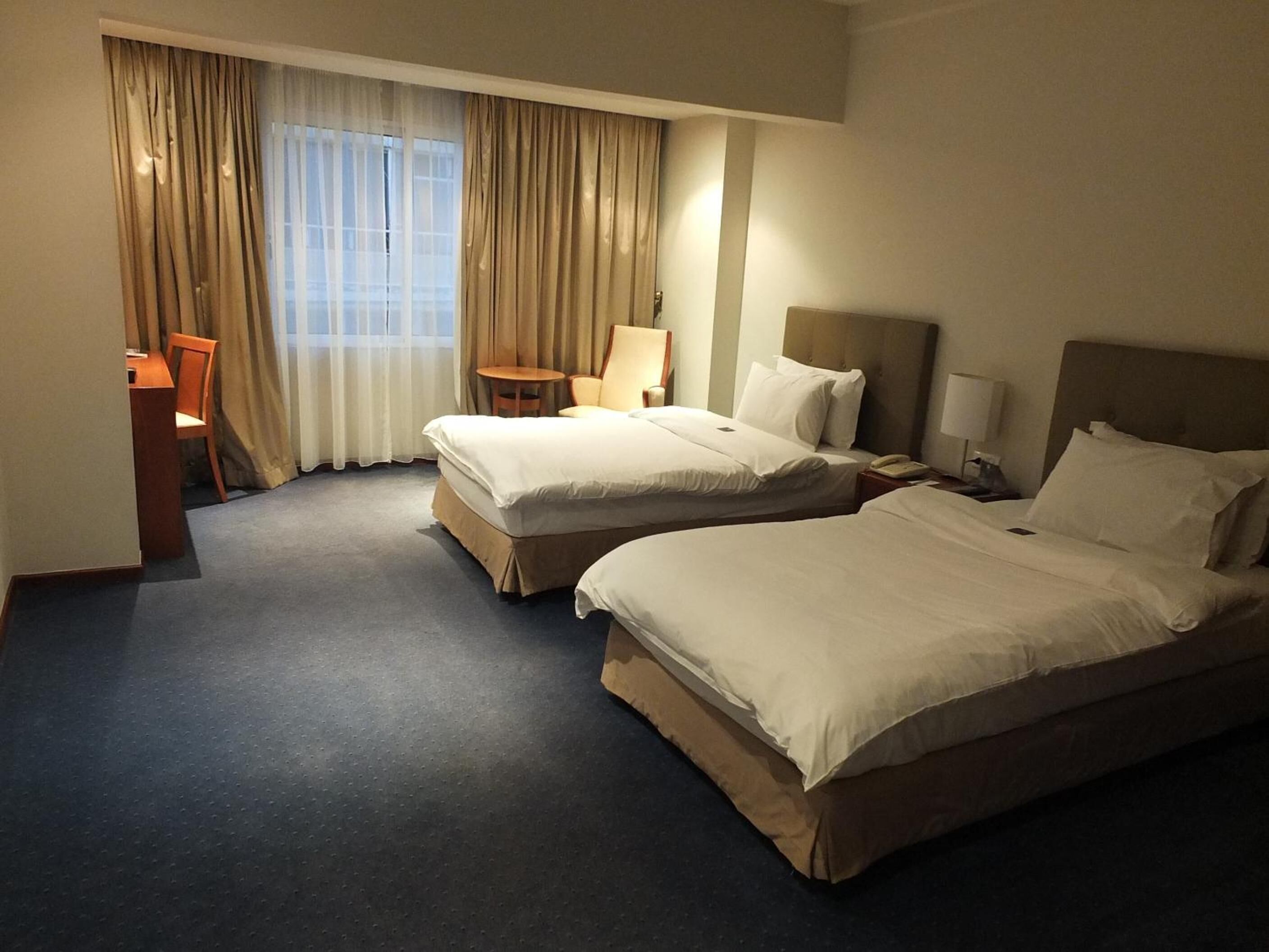 Ett hotellrum med två sängar, ett skrivbord, en stol och ett fönster med gardiner.