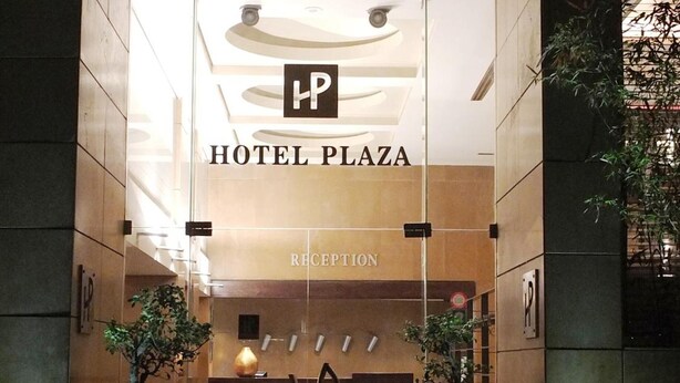 The entrance to a hotel plaza with a reception desk, potted plants, and a clear sign indicating the hotel's name. - Plaza Hotel (Beirut)