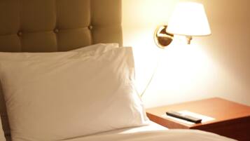 A neatly made bed with a white pillow and a remote control on a wooden nightstand beside it.