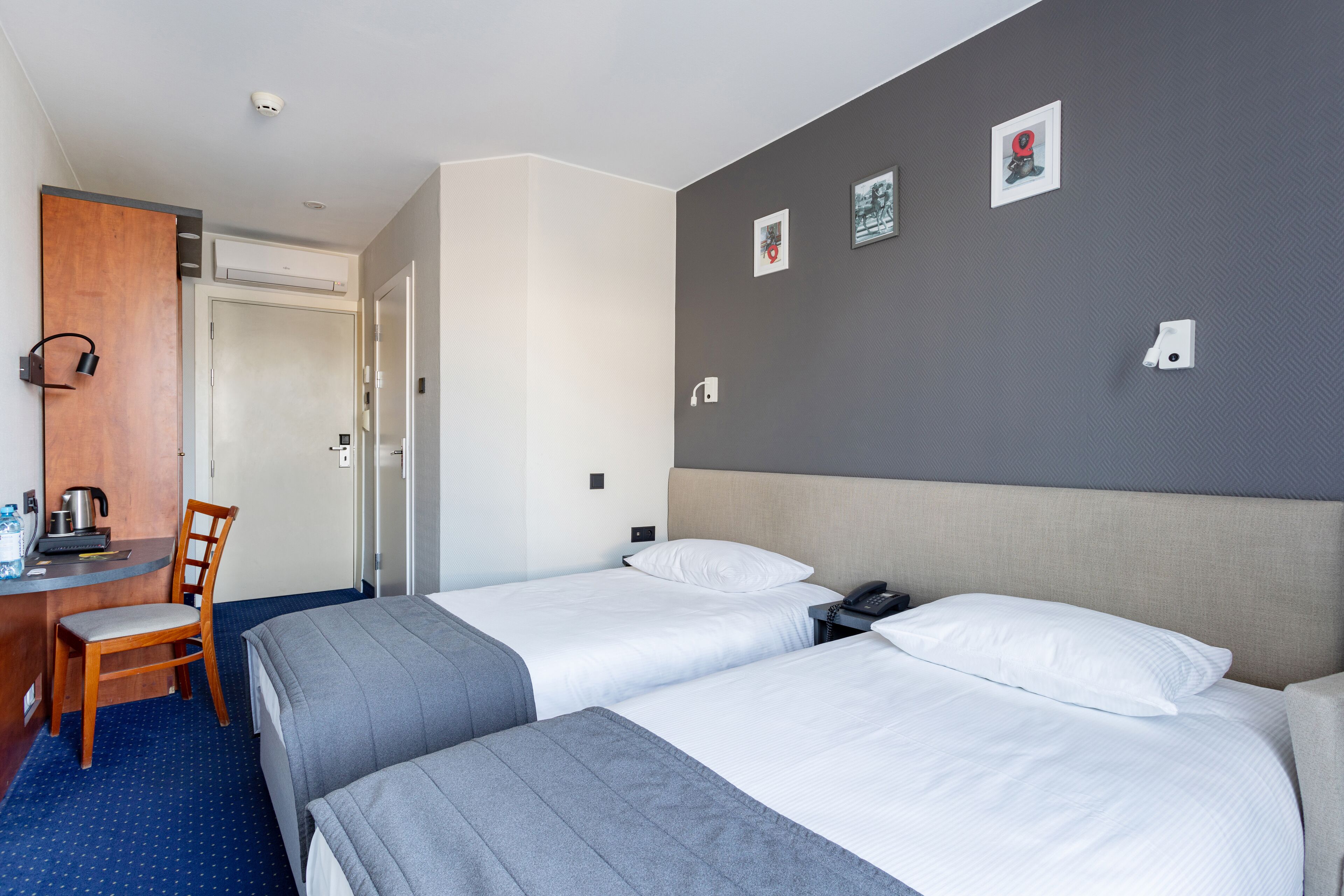 Habitació d'hotel amb dos llits, una taula de treball amb cadira, una cafetera i una porta.