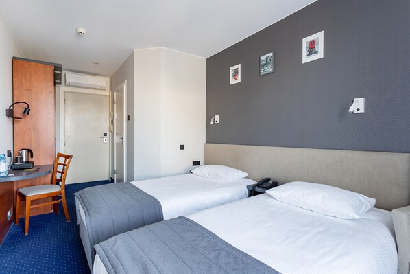 Habitación de hotel con dos camas, un escritorio con silla, una cafetera y una puerta.