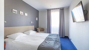 Une chambre d’hôtel avec un grand lit, une chaise, un téléviseur à écran plat fixé au mur et une fenêtre avec des rideaux.