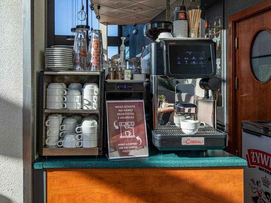 Een koffieapparaat met een bordje in een vreemde taal, bekers en borden op een aanrecht.