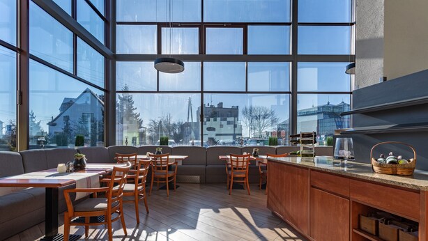 A modern kitchen with large windows, wooden furniture, and a view of the cityscape. - Qubus Hotel Zielona Gora (Zielona Gora)