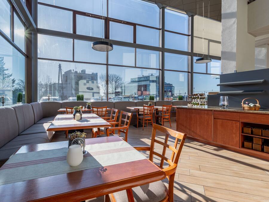 En modern restaurang med stora fönster, träbord och en bardisk.
