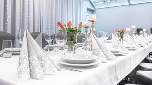 A long dining table set with white tablecloths, silverware, and glassware, with a vase of orange flowers and a candle centerpiece. - Qubus Hotel Zielona Gora (Zielona Gora)
