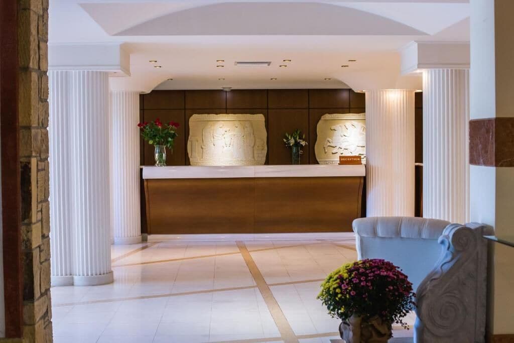A reception area with a marble reception desk, white columns, and a vase with flowers.