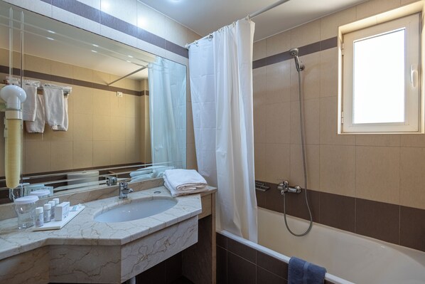 A bathroom with a marble sink, a mirror, a shower, and a window.