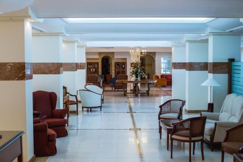 A spacious lobby with a central dining area, multiple seating options including armchairs and sofas, and a chandelier.