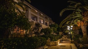 Una vista nocturna de un edificio con balcón, rodeado de vegetación y palmeras.