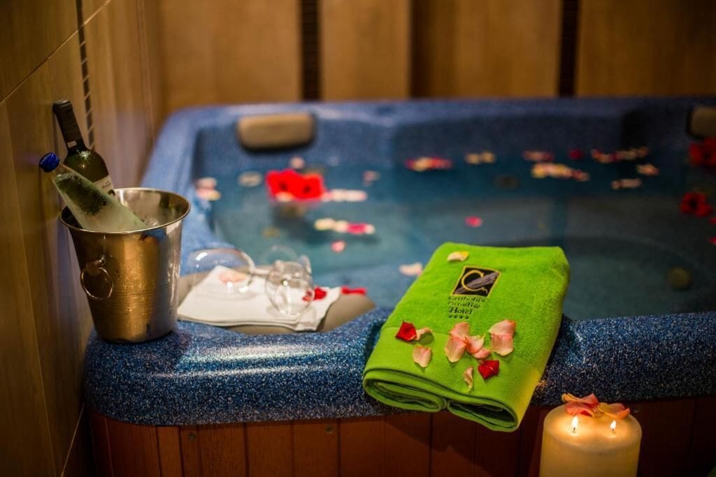 A spa area with a hot tub, a bucket with a bottle, a towel, and a candle.