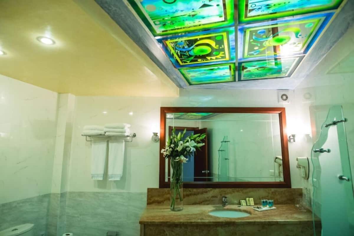 A bathroom with a marble floor, a sink with toiletries, a mirror, and a ceiling with colorful glass panels.
