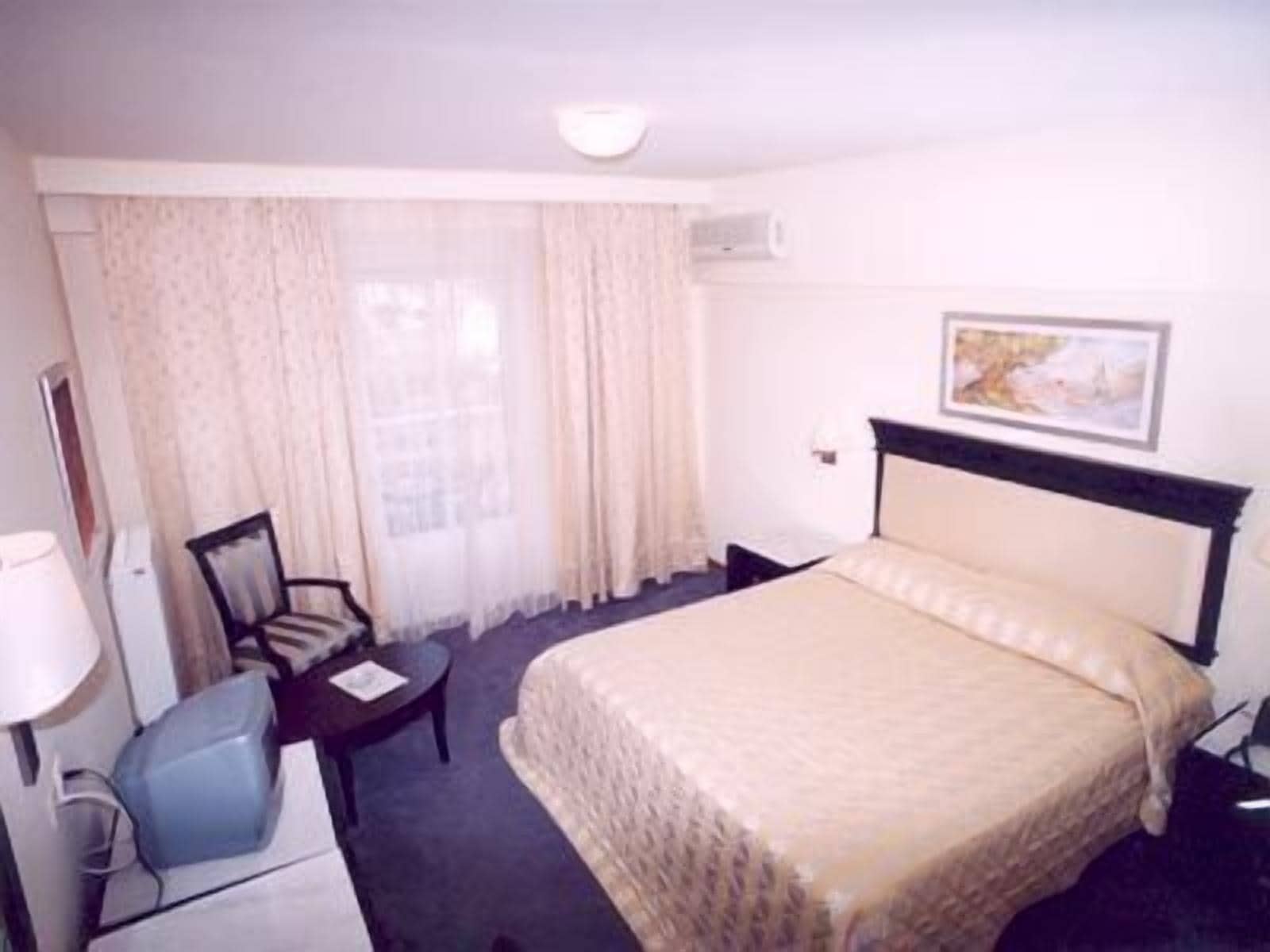 Ein Hotelzimmer mit Bett, Schreibtisch, Stuhl, Lampe und einem Bild an der Wand.