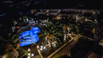 A resort with a large swimming pool, palm trees, and a well-lit outdoor area.
