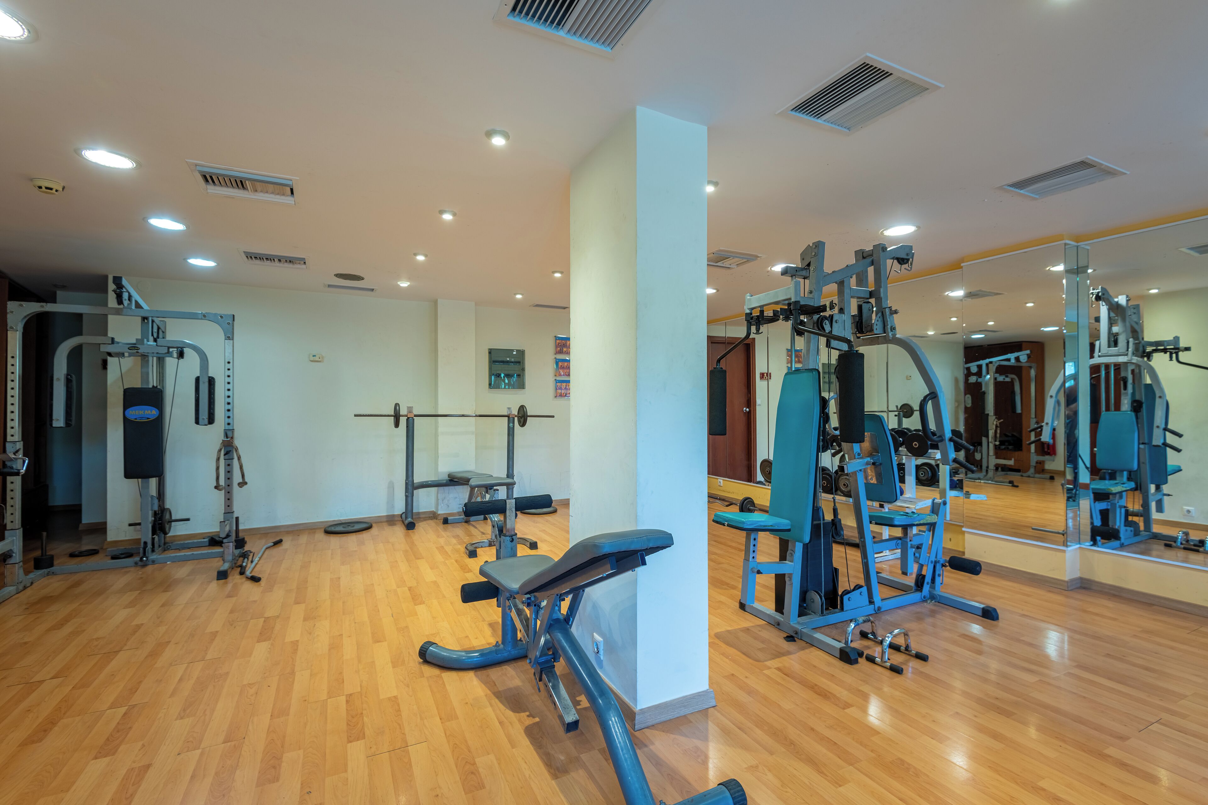 Un gimnasio con equipo de ejercicio, piso de madera y un espejo grande.