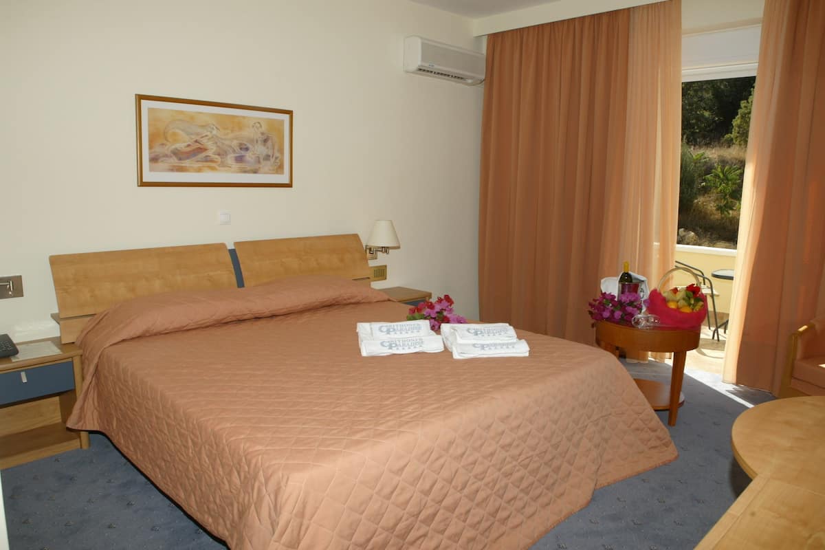 A hotel room with a bed, a nightstand, a lamp, a framed picture on the wall, and a window with curtains.