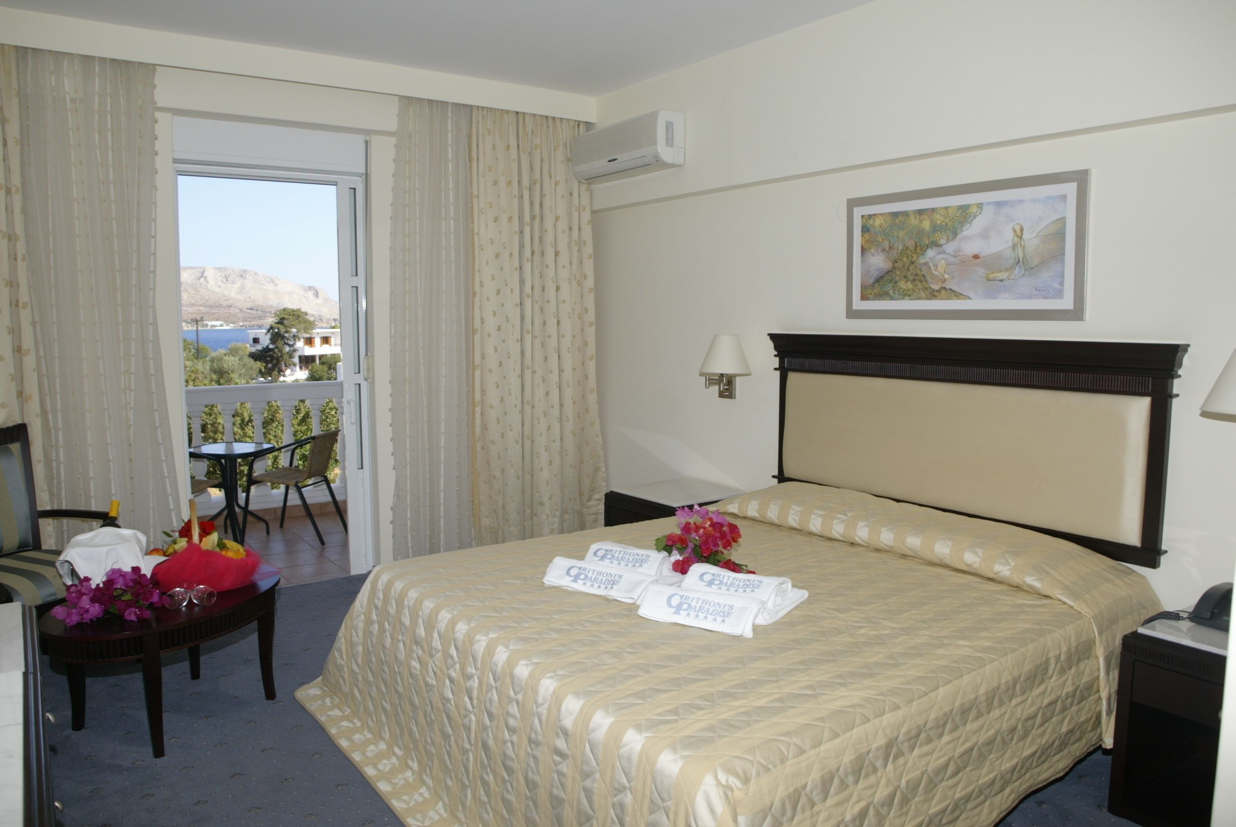 Une chambre d’hôtel avec un lit, un bureau et une chaise, une table ornée d’un vase de fleurs, et une vue sur l’extérieur.