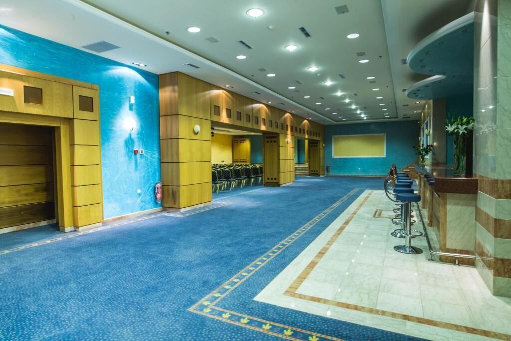 A spacious hotel lobby with a blue carpet, wooden lockers, a reception desk, and a seating area.