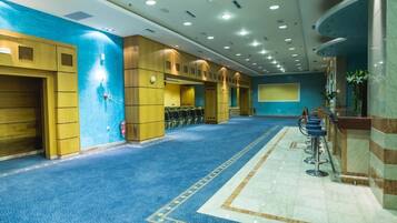 A spacious hotel lobby with a blue carpet, wooden lockers, a reception desk, and a seating area.