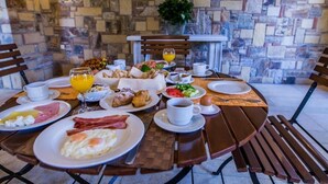Una mesa de desayuno servida con platos de huevos, tocino, pastelería y fruta, junto con tazas y un vaso de zumo de naranja.